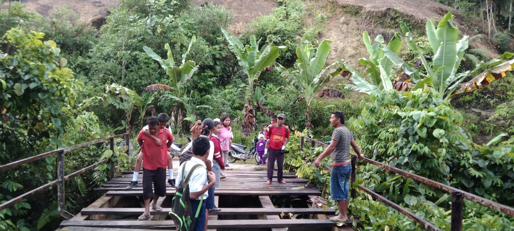 Orangtua terpaksa menggendong anak SD saat melintasi di atas jembatan Lae Suhar Desa Lae Rambong Kecamatan Silima Pungga-Pungga Kabupaten Dairi yang mengalami kerusakan parah. ( DETEKSI.co/istimewa)