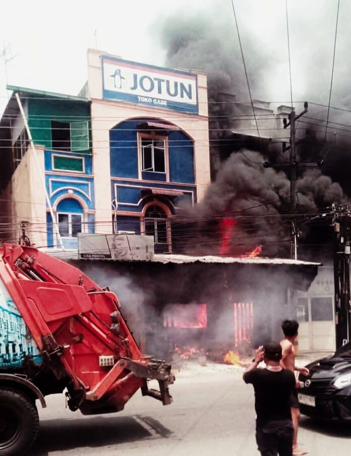 Kobaran api melalap ruko cat berlantai tiga di kawasan Marelan Pasar V, Medan, Kamis (9/4/2026), disertai kepulan asap tebal dan ledakan saat petugas pemadam kebakaran berupaya menjinakkan api.